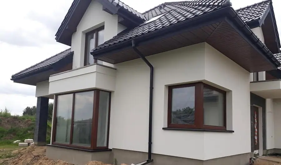 Dom z jasną elewacją i brązową podsufitką pod okapem dachu