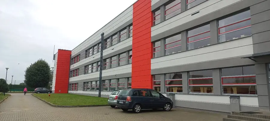 Trzykondygnacyjny budynek z jasnoszarą elewacją i czerwonymi pionowymi akcentami