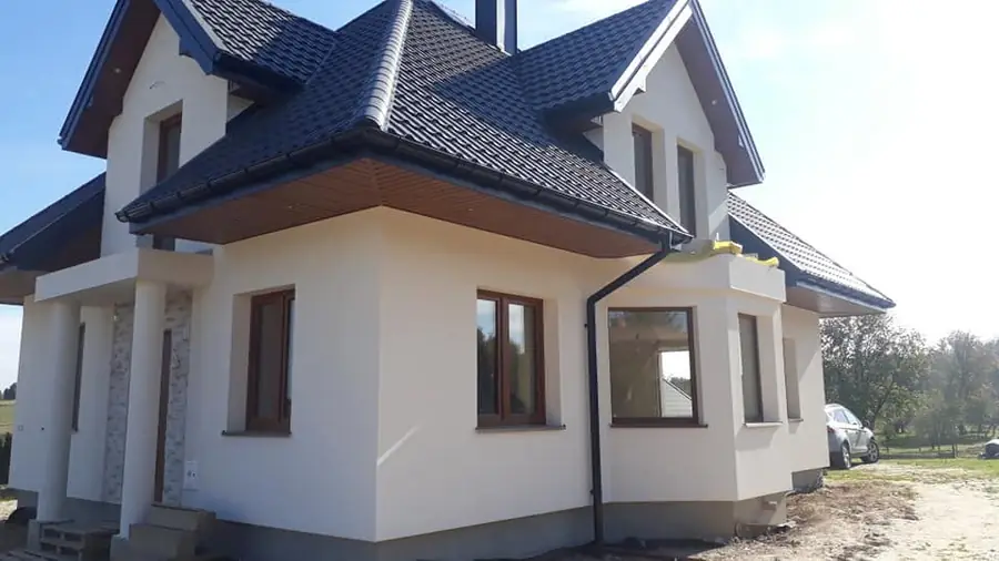 Dom z jasną elewacją, brązową podsufitką i ciemnym dachem